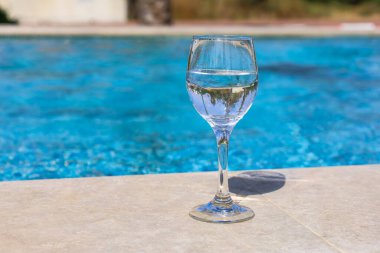 Glass of water near swimming pool, closeup