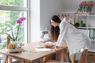 Female tailor drawing sketch at table in atelier