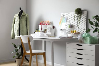 Tailor's workplace with sewing machine, pegboard and tablet computer in atelier