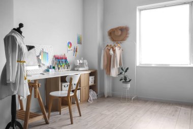 Interior of modern atelier with workplace, mannequin and clothes