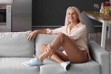 Evdeki kanepede oturan olgun bir kadın.