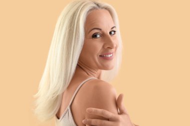 Mature blonde woman smiling on beige background