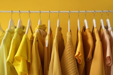 Rack with stylish female clothes near yellow wall, closeup