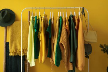 Rack with stylish female clothes and accessories near yellow wall