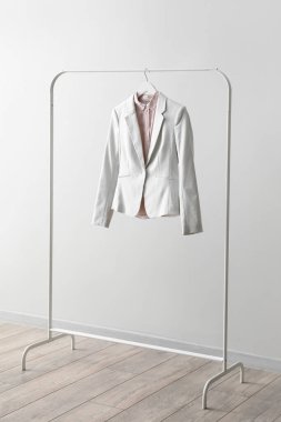 Rack with female jacket and shirt near light wall