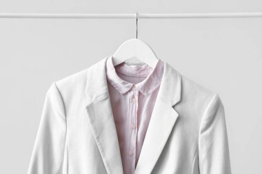 Rack with female jacket and shirt near light wall, closeup