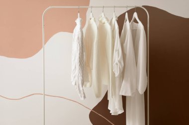 Rack with white female clothes near color wall