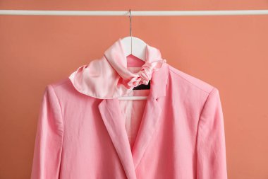 Rack with stylish jacket and scarf near pink wall, closeup