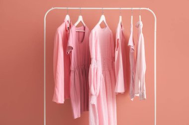 Rack with female clothes near pink wall