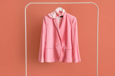 Rack with stylish jacket and scarf near pink wall