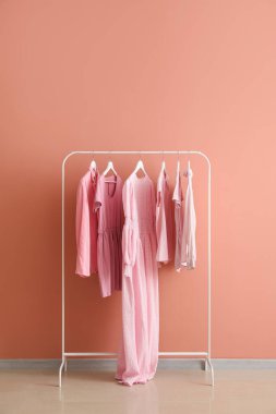 Rack with female clothes near pink wall