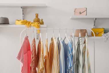 Rack with striped clothes, shelves and accessories on light wall