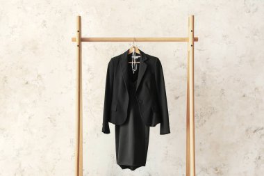 Rack with black female suit near light wall