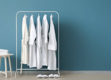 Rack with white bathrobes and sleepers near color wall