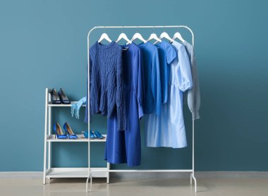 Rack with blue clothes and shoe stand near color wall