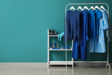 Rack with blue clothes and shoe stand near color wall