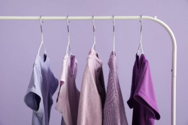 Rack with stylish clothes near lilac wall, closeup