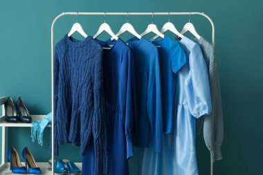 Rack with blue clothes and shoe stand near color wall