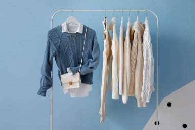 Rack with stylish clothes and bag near color wall
