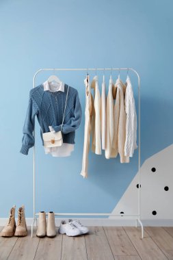 Rack with stylish clothes, bag and shoes near color wall