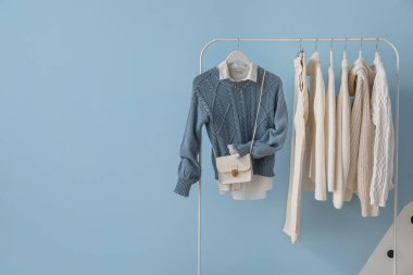 Rack with stylish clothes and bag near color wall