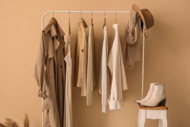 Rack with stylish clothes, table and shoes near beige wall