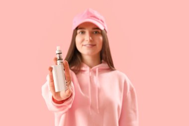 Young woman in cap with disposable electronic cigarette on pink background, closeup