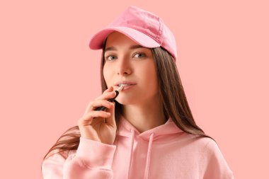Young woman in cap with disposable electronic cigarette on pink background, closeup