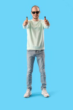 Young man in sunglasses with disposable electronic cigarettes on blue background