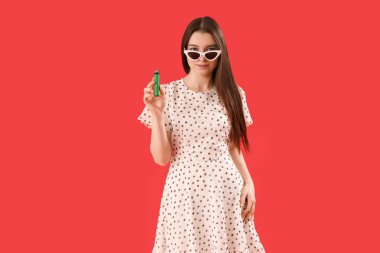 Young woman in sunglasses with disposable electronic cigarette on red background