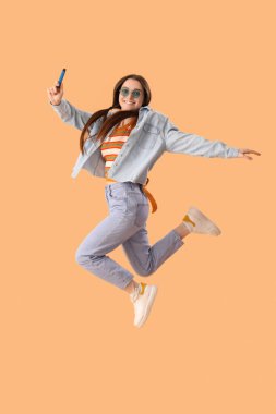 Young woman in sunglasses with disposable electronic cigarette jumping on beige background