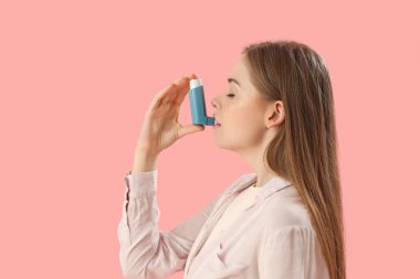 Sick young woman with inhaler on pink background
