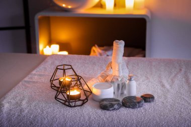 Spa composition with burning candles on couch in dark salon, closeup