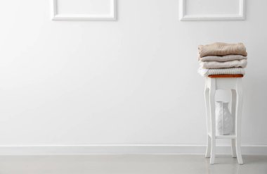 Folded knitted sweaters on table near light wall