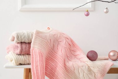 Knitted sweaters and Christmas balls on table near light wall, closeup