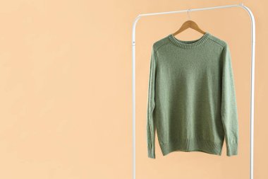 Rack with green sweater on beige background