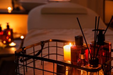 Basket with cosmetic products, burning candles and reed diffuser in dark spa salon, closeup