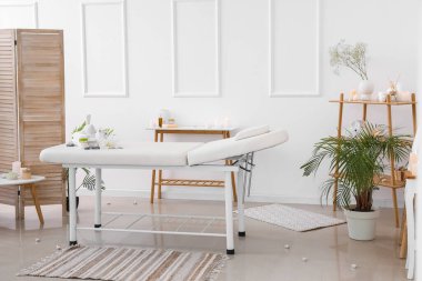 Interior of light spa salon with couch, burning candles and palm trees