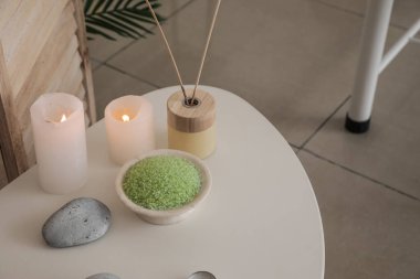 Spa composition with burning candles and reed diffuser on table in salon, closeup
