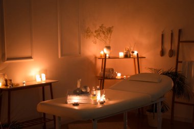 Interior of dark spa salon with couch, burning candles and table
