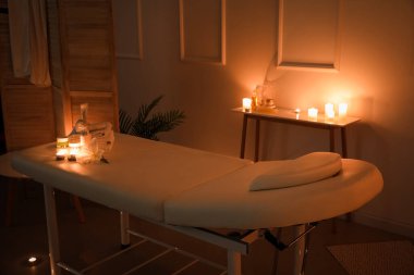 Interior of dark spa salon with couch, burning candles and table