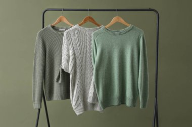 Rack with knitted sweaters on green background