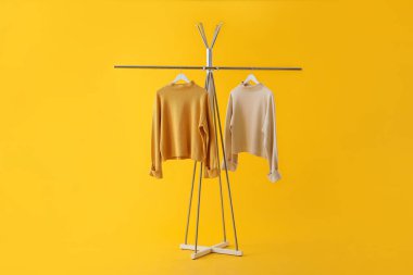 Rack with stylish sweaters on yellow background