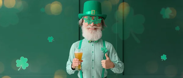 Happy senior man with big head and glass of beer showing thumb-up gesture on green background. St. Patrick\'s Day celebration