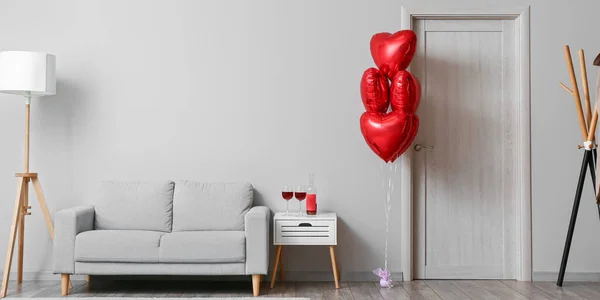 Interior of living room with red heart shaped balloons, table with wine and sofa. Valentine\'s Day celebration
