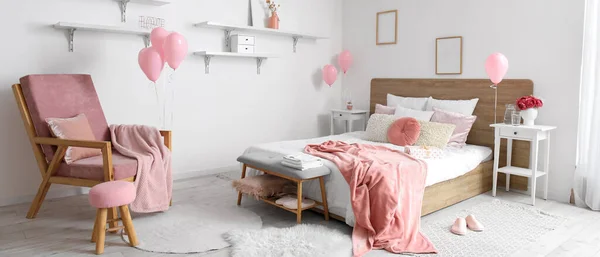 Interior of light bedroom with armchair and pink balloons for Valentine\'s Day