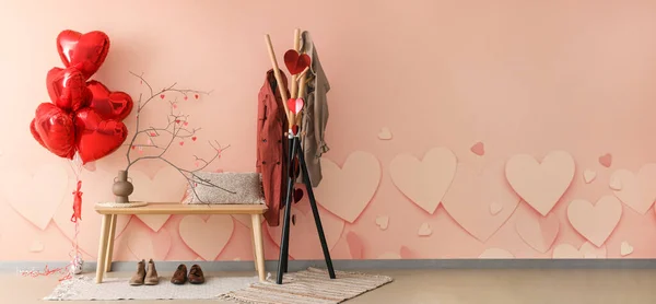 Wooden bench, rack with clothes and red balloons near pink wall with printed hearts in hall. Valentine\'s Day celebration