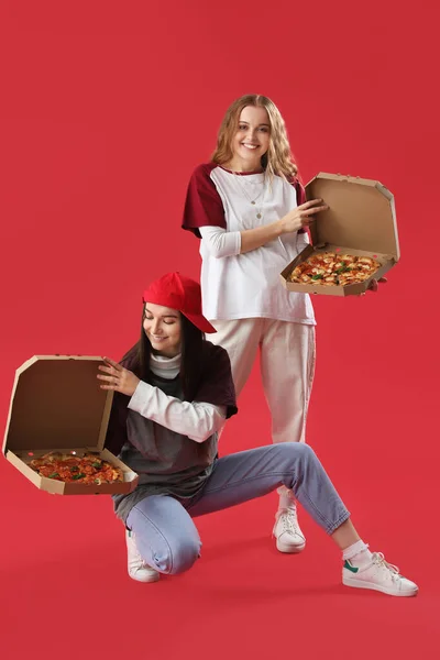 Young women with boxes of tasty pizza on red background