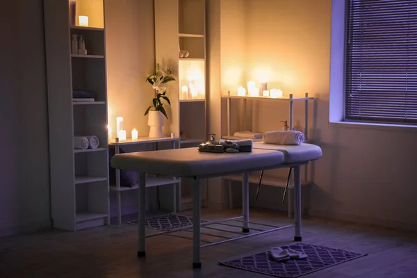Interior of dark spa salon with couch, shelving units and burning candles