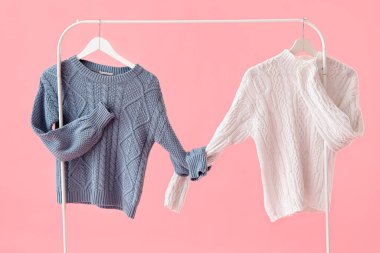 Rack with knitted sweaters on pink background